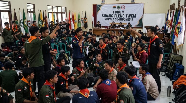 Foto ilustrasi situasi ramai dan penuh interaksi di dalam ruang sidang "Forum Sidang Pleno TWKM Mapala se-Indonesia". Ratusan peserta mahasiswa pecinta alam (Mapala) mengenakan jaket lapangan (PDL) dan slayer merah-oranye duduk berkerumun di lantai serta kursi plastik sambil berdiskusi dengan intens. Tampak spanduk di dinding bertuliskan "FORUM SIDANG PLENO TWKM MAPALA SE-INDONESIA" dengan jajaran bendera organisasi di bagian belakang. Beberapa peserta berdiri sambil mengacungkan tangan dan berbicara menggunakan mikrofon di tengah kerumunan yang padat.